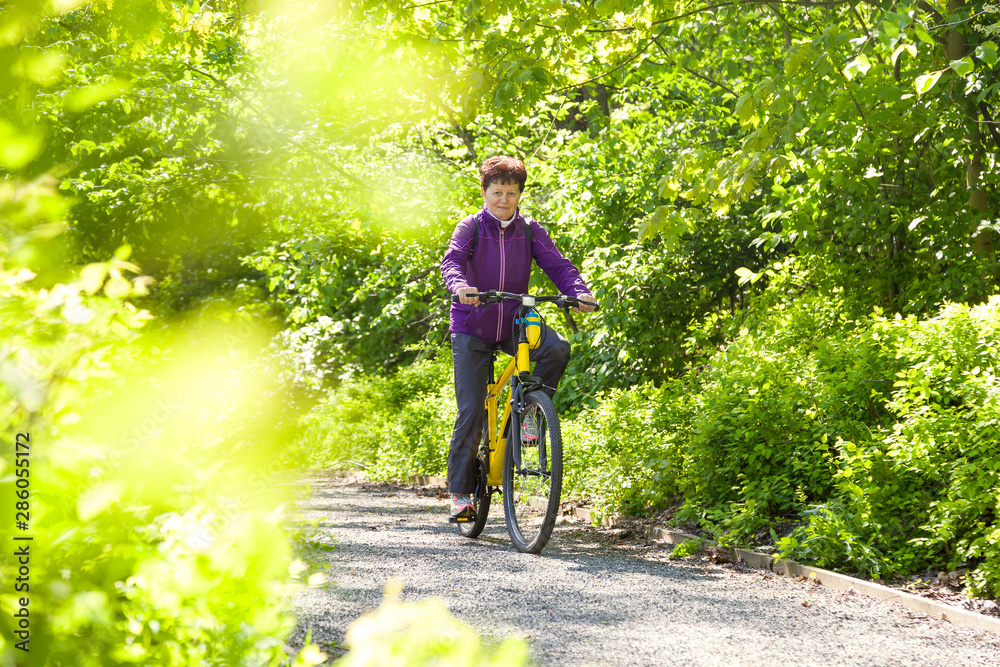 Naklejka premium Happy beautiful senior woman riding a bike in summer park
