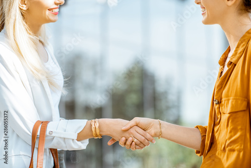 Two businesswomen having a deal shaking handsoutdoors, close-up view