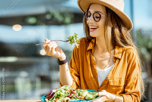 Foto Stylish young woman eating healthy salad on a restaurant terrace, feeling happy