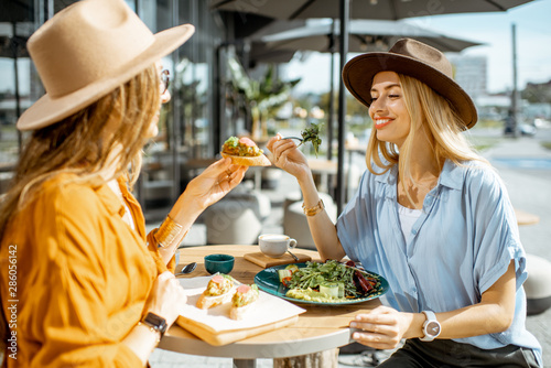Two female best friends eating healthy food while sitting together on a restaurant terrace on a summer day