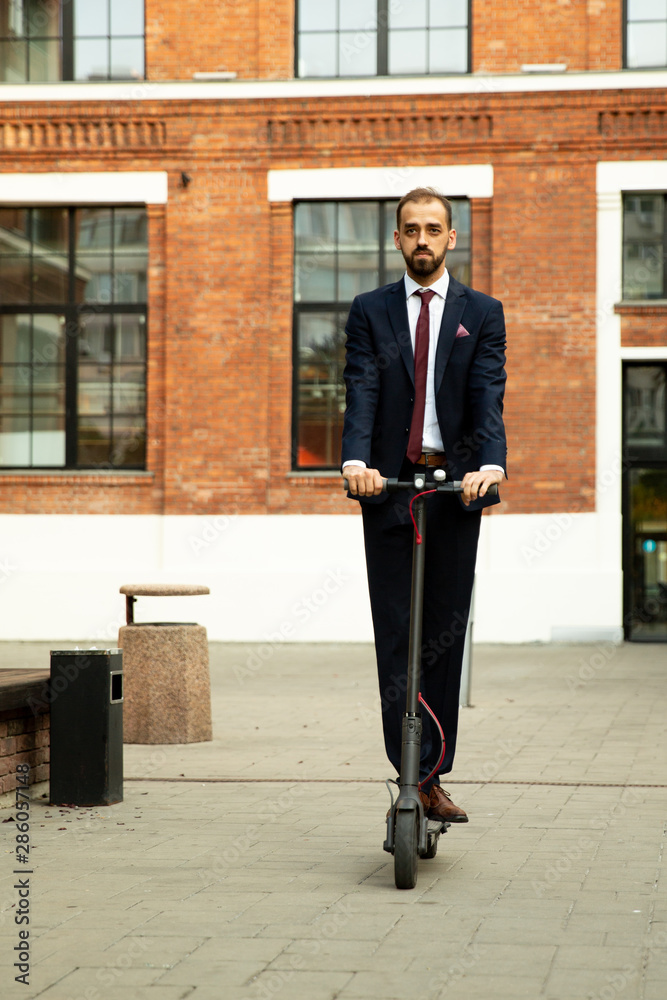 Young businessman in a suit riding an electric scooter in a business district Young businessman in a suit riding an electric scooter in a business district