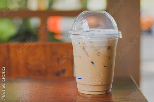 Side view Ice coffee (cappuccino, latte, mocha) in plastic cup with water drop on wooden column with blurry garden background with copy space for your text. Vintage tone