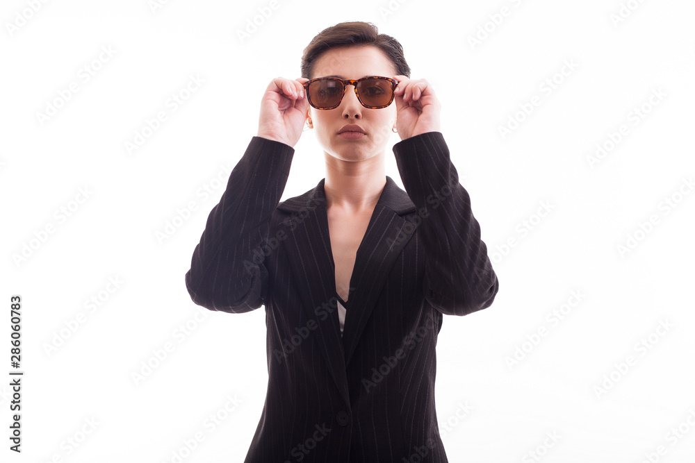 Beautiful young model posing with sunglasses and wearing a black jacket over white background in studio Beautiful young model posing with sunglasses and wearing a black jacket over white background in studio