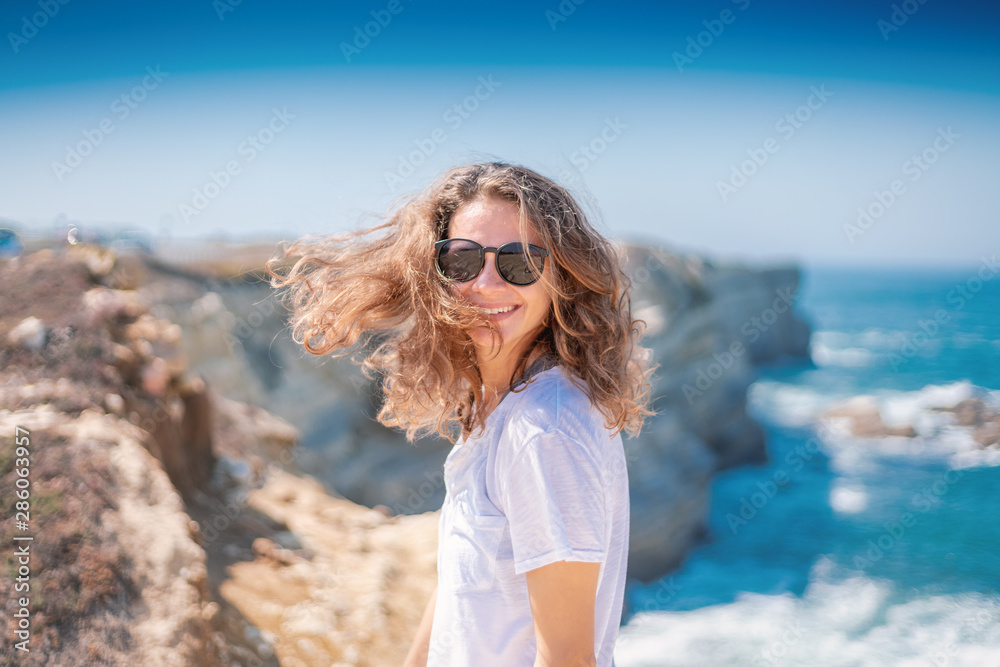 Beautiful young woman with a happy smile in a white T-shirt on the ocean in Portugal Beautiful young woman with a happy smile in a white T-shirt on the ocean in Portugal
