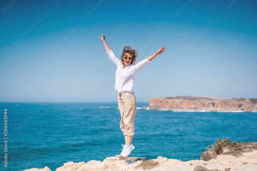 Beautiful young woman with a happy smile in a white shirt on the ocean in Portugal Beautiful young woman with a happy smile in a white shirt on the ocean in Portugal