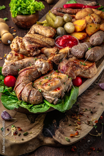 Assorted meat. A large beautiful wooden plateau with juicy pieces of pork, beef, chicken, meat.  Grilled sausages, bones, ribs, fillets, barbecue with appetizer of pickles and potatoes. 