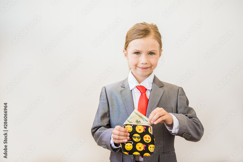 Happy child girl stands in a fashionable suit with a purse in her hands. Success, creative and innovation business concept Happy child girl stands in a fashionable suit with a purse in her hands. Success, creative and innovation business concept