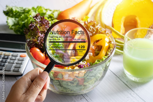 nutritional information concept. hand use the magnifying glass to zoom in to see the details of the nutrition facts from food , salad bowl photo