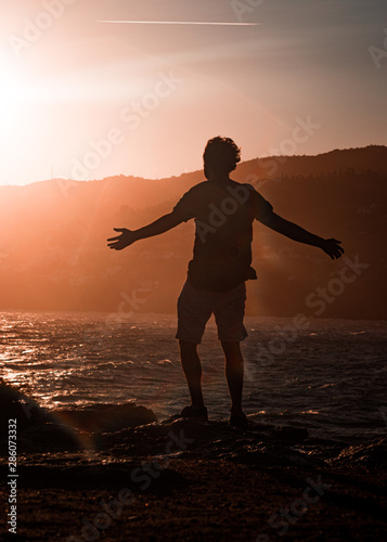 Фотография chico abriendo los brazos frente al mar al atardecer