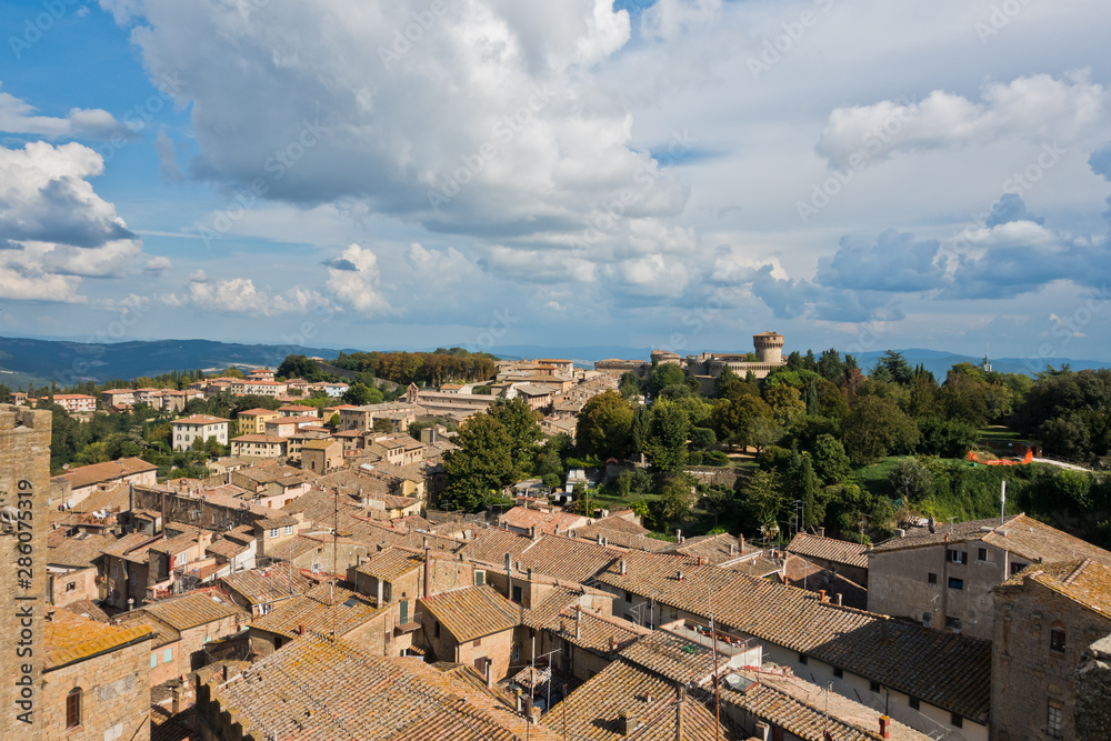 Cityscape of Volterra over the roofs with surrounding landscape, Medici fortress in background, Tuscany, Italy
