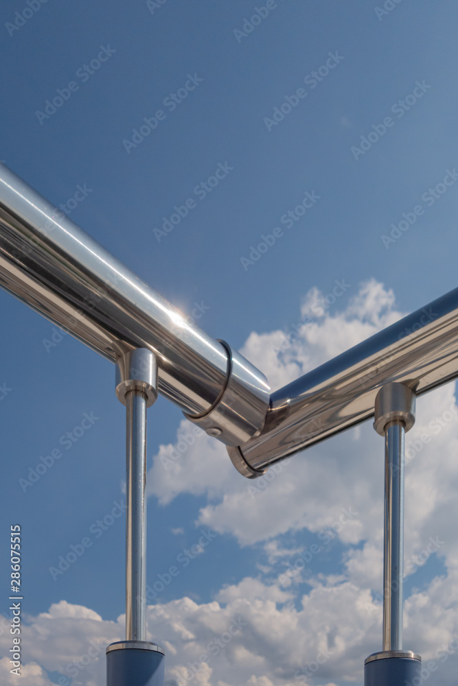 Stainless steel railing stairs from the outside of the building on a background of blue sky and beautiful clouds. Pipes, hinges, balusters made of stainless steel. Stainless steel railing stairs from the outside of the building on a background of blue sky and beautiful clouds. Pipes, hinges, balusters made of stainless steel.