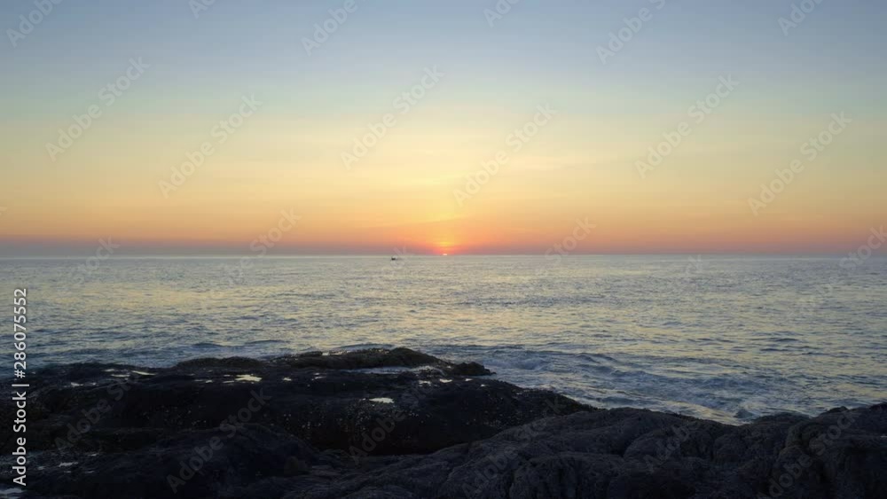 Beautiful blue and purple sunset from a rocky beach with small boat silhouette and sun behind horizon Beautiful blue and purple sunset from a rocky beach with small boat silhouette and sun behind horizon