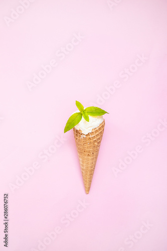Mint vanilla ice cream with in a waffle cone with mint leaves on a pink plain background.