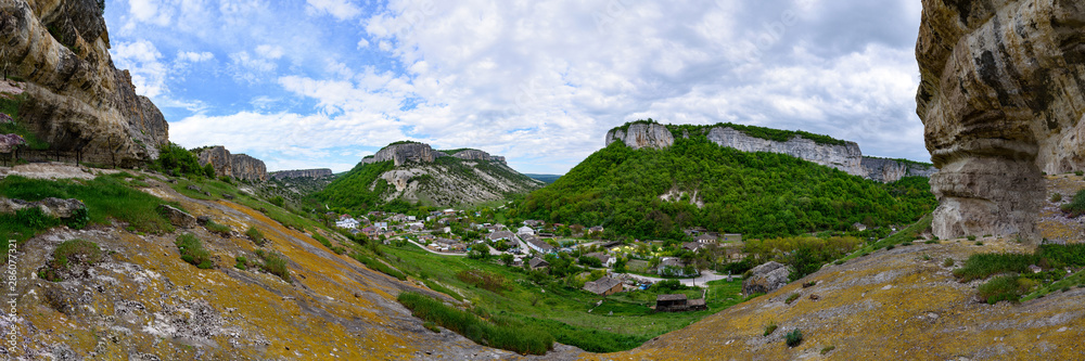 View of the suburb of Bakhchisarai located between two large mountains with flat peaks and having a white color on a sunny day, with clouds in the sky. Spring view of the Crimean mountains.