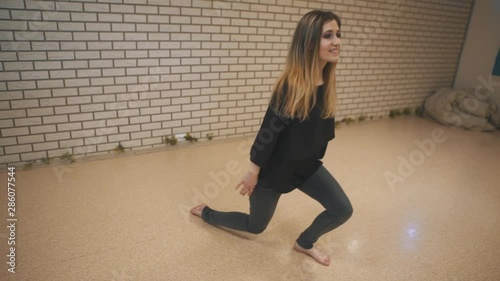 Pretty girl performing dance moves on floor in dance studio. Mid shot