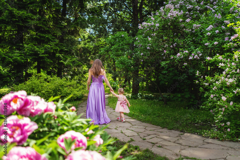 Mother on the walk with little daughter in the garden. Back view Mother on the walk with little daughter in the garden. Back view