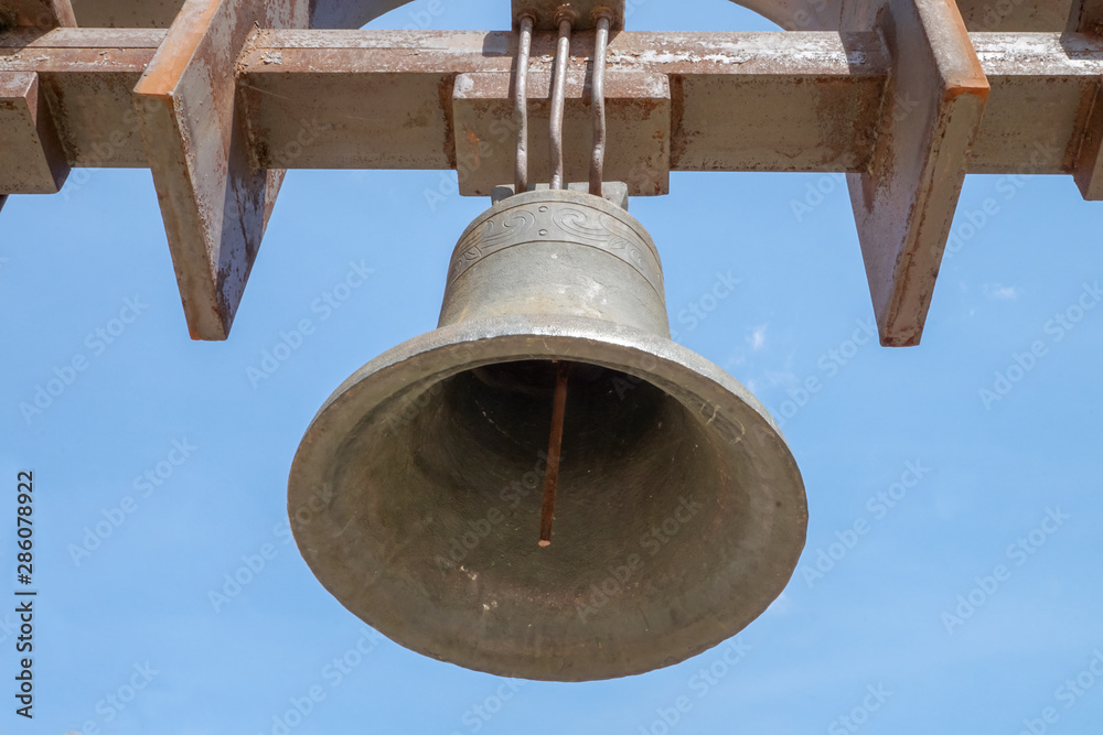 A church bell weighs against a blue sky. Horizontal shot.