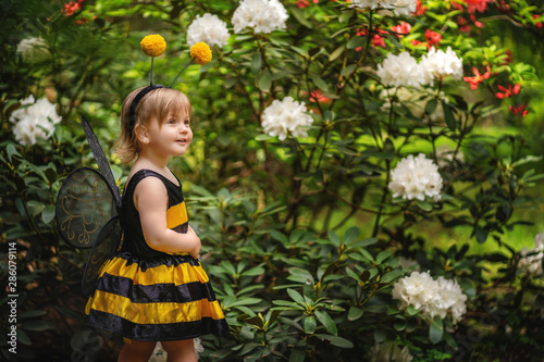 Happy little girl wearing a costume of bee walking near the blooming bush in the park.