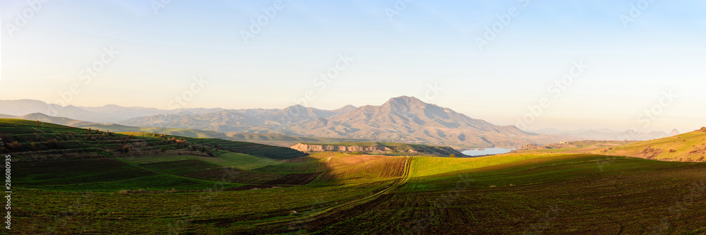 plowed fields look like alpine meadows in the light of the setting sun with mountain ranges and a lake on a clear sunny day.