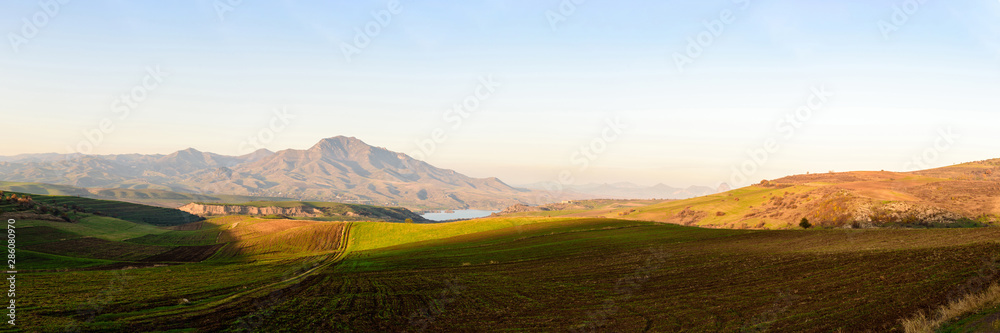 plowed fields look like alpine meadows in the light of the setting sun with mountain ranges and a lake on a clear sunny day.