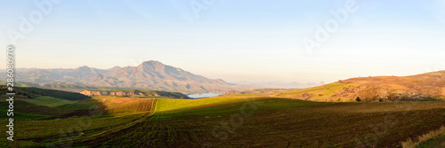 plowed fields look like alpine meadows in the light of the setting sun with mountain ranges and a lake on a clear sunny day.