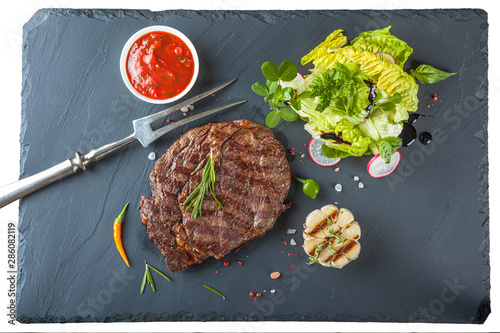 The ribeye steak with sprig of rosemary anh salad on a black stone slab photo