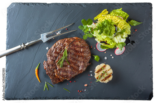 The ribeye steak with sprig of rosemary anh salad on a black stone slab photo