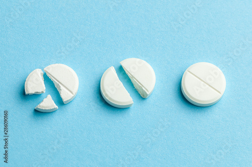 White pills on blue background. Few pills broken in half, reducing the dose of the medicine