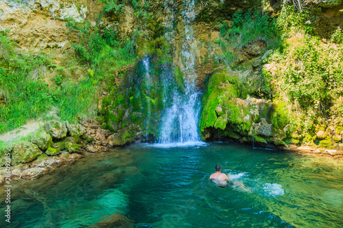 Man swimming in clear and cold water in natural pool under waterfall at forest