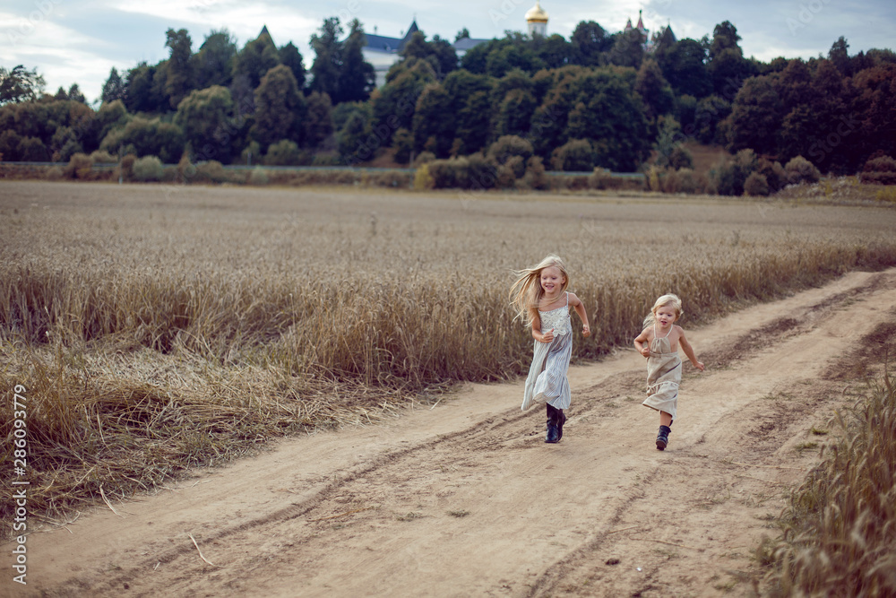 two girls in long dresses running along the path to the field