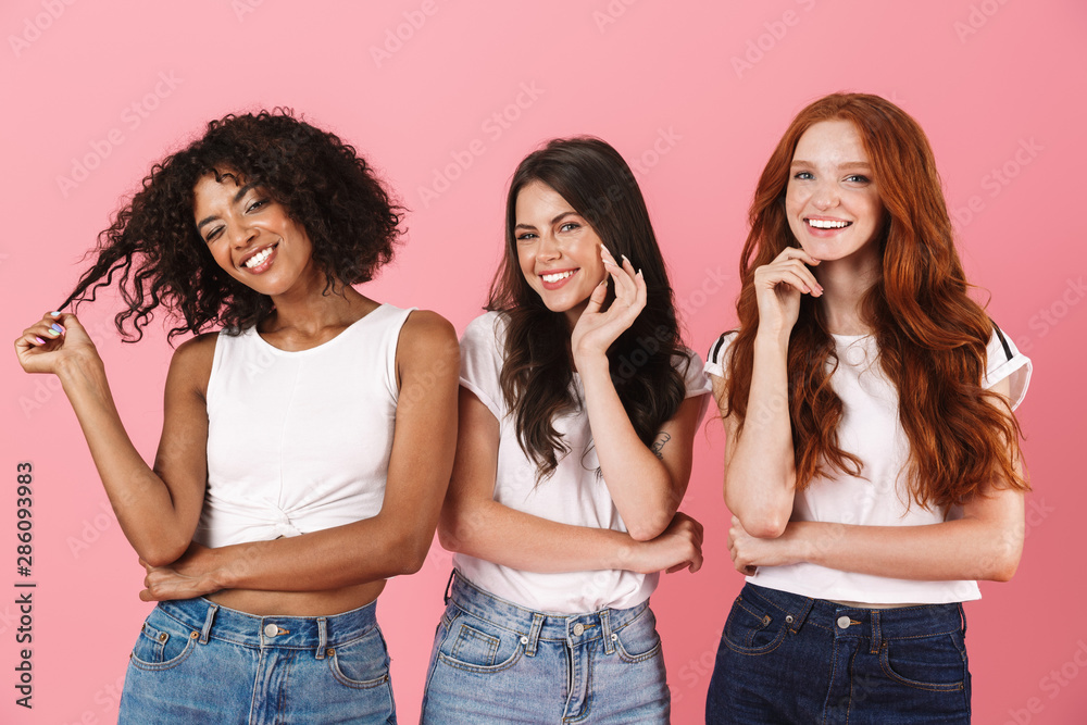 Playful young three multiethnic girls friends posing isolated over pink wall background. Playful young three multiethnic girls friends posing isolated over pink wall background.