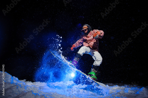 Male snowboarder dressed in a white and pink sportswear performs tricks on the snow slope