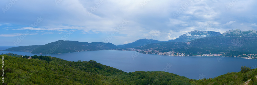 an island in the middle of the Adriatic Sea against the mountains on a sunny day with cumulus clouds on the sky.