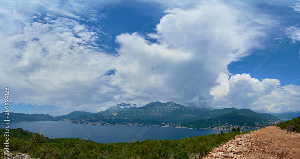 an island in the middle of the Adriatic Sea against the mountains on a sunny day with cumulus clouds on the sky.