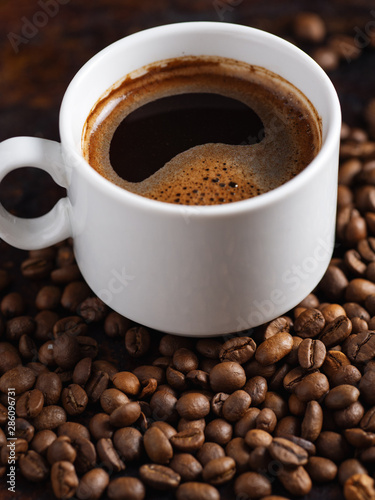 White Cup of espresso close-up on roasted coffee beans