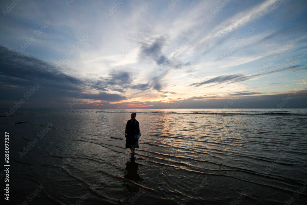 Beautiful summer seaside view of woman standing in Baltic sea in a lovely evening - sunset.