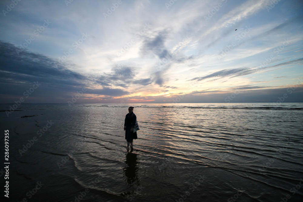 Beautiful summer seaside view of woman standing in Baltic sea in a lovely evening - sunset.