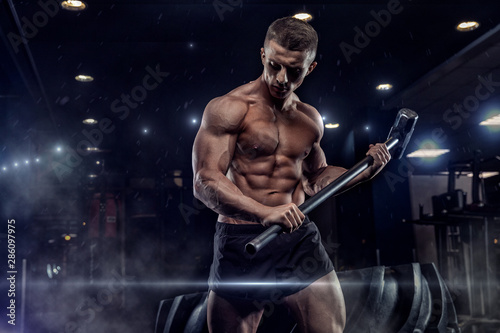 Sport Fitness Man Hitting Wheel Tire With Hammer Sledge Crossfit Training, Young Healthy Guy Gym Interior © romanolebedev