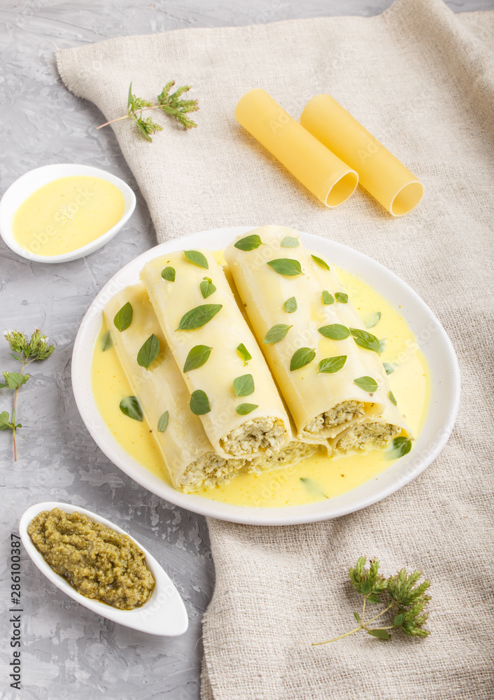 Cannelloni pasta with egg sauce, cream cheese and oregano leaves on a gray concrete background with linen textile. side view Cannelloni pasta with egg sauce, cream cheese and oregano leaves on a gray concrete background with linen textile. side view