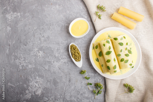 Cannelloni pasta with egg sauce, cream cheese and oregano leaves on a gray concrete background with linen textile. top view
