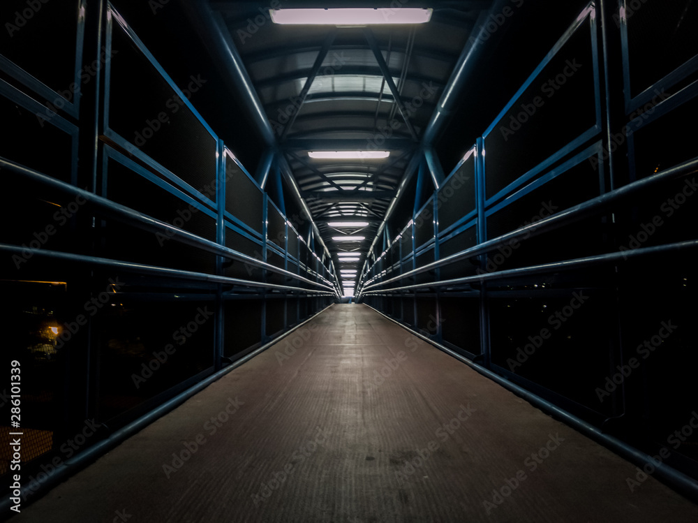 Empty pedestrian walkway illuminated with fluorescent tubes at night. Metallic structure over a road