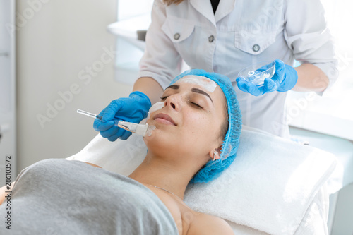 A professional cosmetologist applies a nourishing cream on the patient's face. Moisturizing, cleaning and facial skin care. Cosmetic procedures
