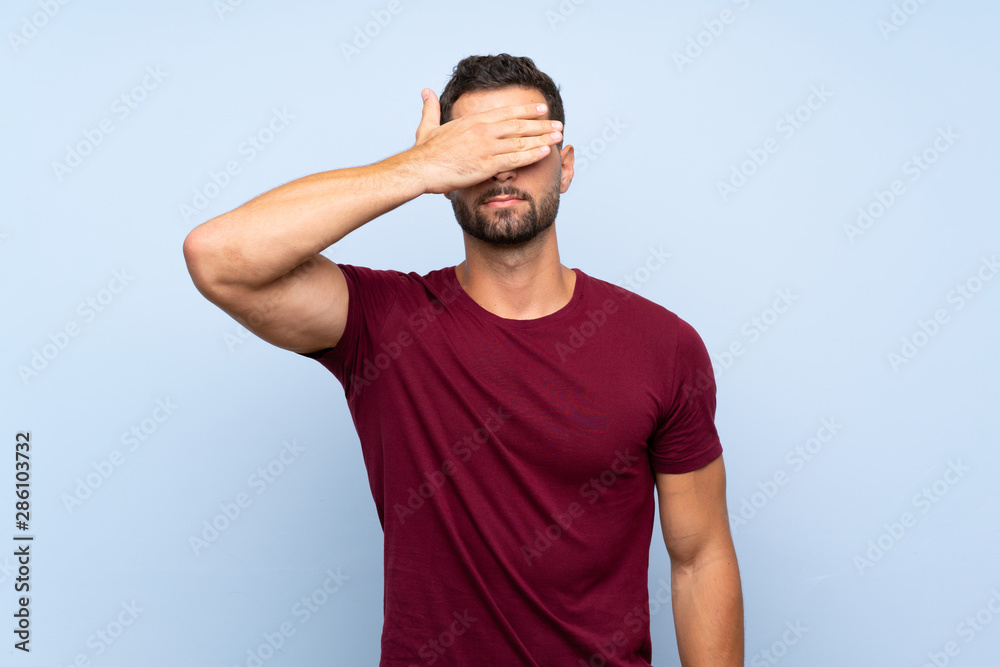 Handsome man over isolated blue background covering eyes by hands. Do not want to see something Handsome man over isolated blue background covering eyes by hands. Do not want to see something