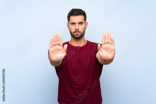 Handsome man over isolated blue background making stop gesture and disappointed