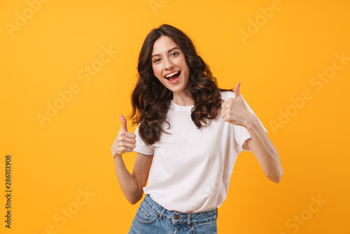 Behang Image of gorgeous brunette woman wearing casual clothes smiling and showing thum