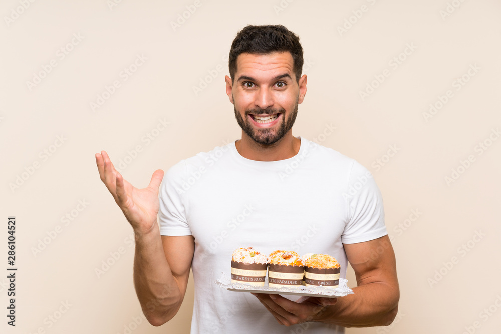 Handsome man holding muffin cake over isolated background with shocked facial expression Handsome man holding muffin cake over isolated background with shocked facial expression