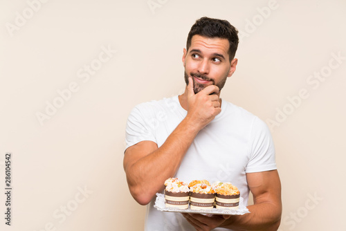 Handsome man holding muffin cake over isolated background thinking an idea