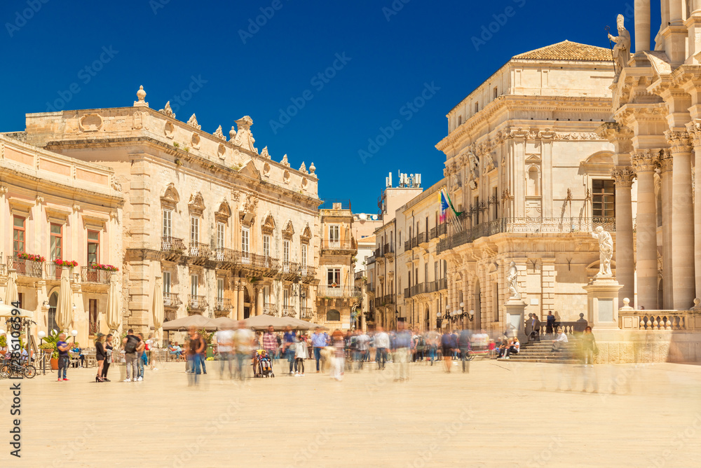 View of The Central Square in Ortygia (Ortigia, Piazza Duomo) with walking people. Historical buildings in the famous Sicilian town Syracuse (Siracusa), Italy