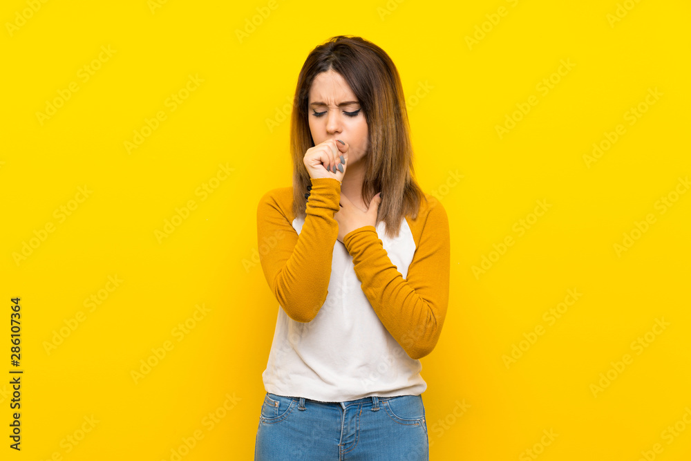 Pretty young woman over isolated yellow wall is suffering with cough and feeling bad Pretty young woman over isolated yellow wall is suffering with cough and feeling bad