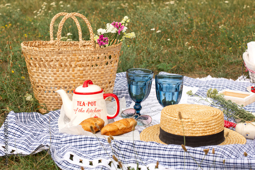 Stylish picnic on the green lawn. Fresh croissants and a teapot with tea on a bedspread near a wicker female hat. Instagram content